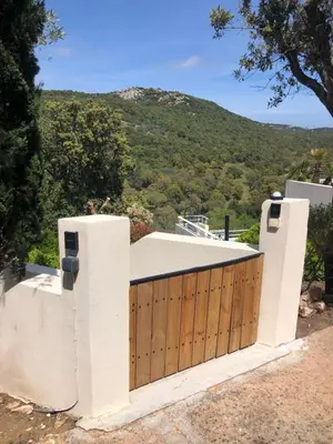 a house with a wooden gate with a mountain in the background at T2 entre Mer et Montagnes in Porto-Vecchio