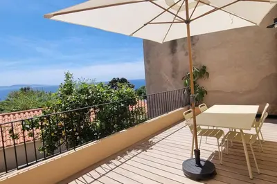 a white table and an umbrella on a balcony at Appartement avec terrasse au centre du village in Cargèse