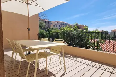 a white table and chairs on a balcony with an umbrella at Appartement avec terrasse au centre du village in Cargèse