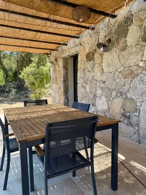 a wooden table and chairs on a patio with a stone wall at Villa de charme avec piscine in Sotta