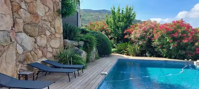 a swimming pool with two chairs next to a stone wall at La baie des anges in Porto-Vecchio