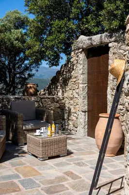 a patio with a table and a chair and a stone wall at Hôtel Case Latine in Lama