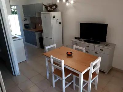 a kitchen with a wooden table with chairs and a television at Villa, maison bord de mer climatisée in Poggio-Mezzana