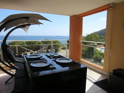 a table with glasses and an umbrella in front of a window at Bel app T2 en bord de Mer vue Sanquinaires piscine in Ajaccio