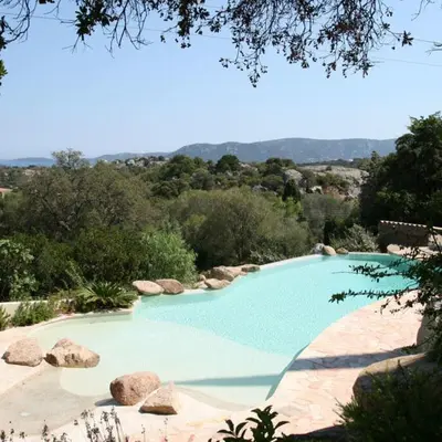 a large blue swimming pool with rocks and trees at Chambre Shelby vue mer avec kitchenette in Porto-Vecchio