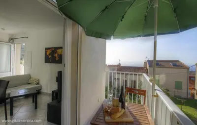 a living room with a balcony with a green umbrella at Idéal logement Cargese 4 in Cargèse