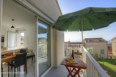 a patio with a table and an umbrella on a balcony at Idéal logement Cargese 4 in Cargèse