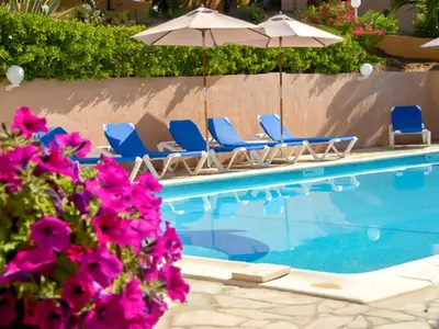 a swimming pool with chairs and umbrellas and purple flowers at Apartment Residence Cabanaccia 3 Pieces 4 Pers by Interhome in Serriera