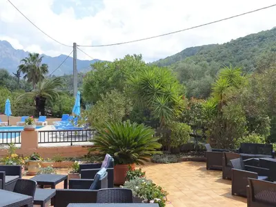 a patio with tables and chairs and mountains in the background at Apartment Residence Cabanaccia 3 Pieces 6 Pers-3 by Interhome in Serriera