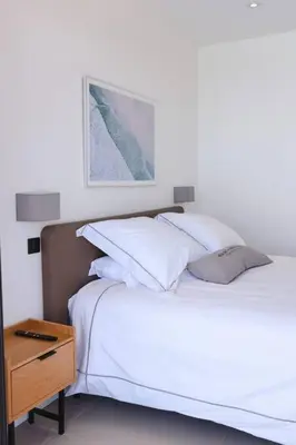 a bed with white sheets and pillows next to a table at Villa luxe avec piscine et belle vue mer in Pietrosella