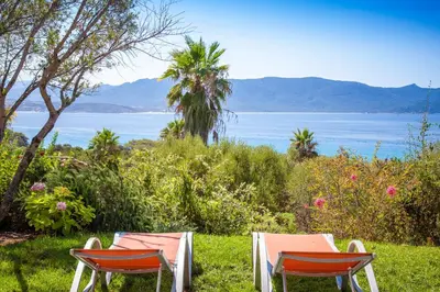 two chairs sitting in the grass near the water at Résidence Cantu di Mare in Olmeto
