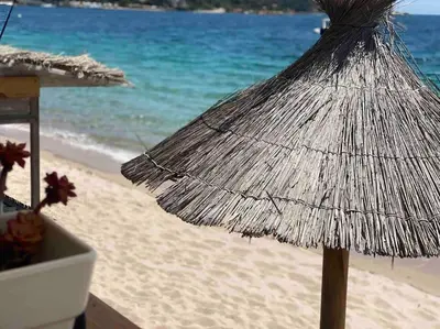 a straw umbrella on the beach near the ocean at Villa piscine à 1km plage proche porto vecchio in Lecci