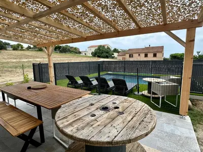 a wooden table and chairs under a wooden pergola at Casa Lamaghjone - Villa T4 avec piscine chauffée à 3,5km de la mer in Aléria