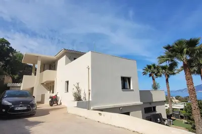 a white house with a car parked in front of it at Appartement terrasse et vue mer in Grosseto-Prugna