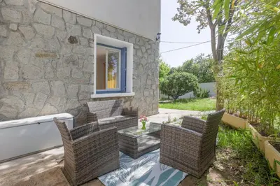 a patio with wicker chairs and a stone wall at Terrazza Moriani - Charmant appartement à 500m de la mer in San-Nicolao