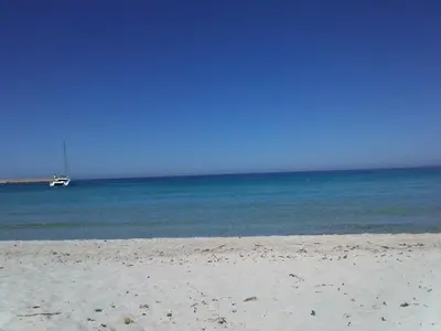 a view of a beach with a boat in the water at La Corse mer turquoise et sable fin in Poggio-Mezzana