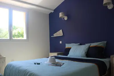 a bedroom with a blue wall with a bed and a window at MINI VILLA PALOMBAGGIA - Piscine chauffée in Porto-Vecchio