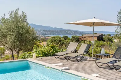 a swimming pool with two chairs and an umbrella at Les Villas de Lorello in Porticcio