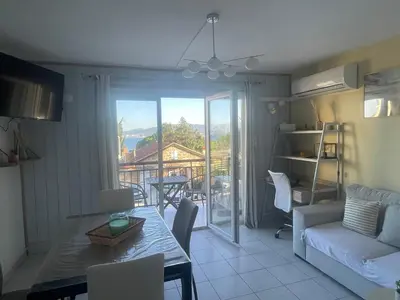 a living room with a table and a view of a balcony at Appartement cosy, vue mer à 5 min à pied de la mer in Grosseto-Prugna
