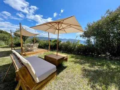 a bed and an umbrella in the grass at Maison en bord de mer in Coggia