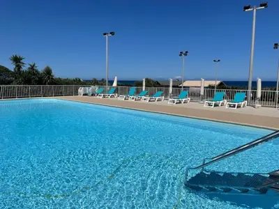 a large swimming pool with blue chairs and the ocean at A 5 mn à pied de la mer, piscine ,tennis, paillote in Cervione
