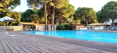 a swimming pool with an umbrella and a wooden deck at Studio grande piscine dans résidence hôtelière, proche plage in Lecci