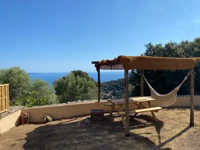 a hammock and a table with a view of the ocean at Magnifique Bergerie RONDOLINO vue mer et montagne - U Sognu di Paomia in Cargèse