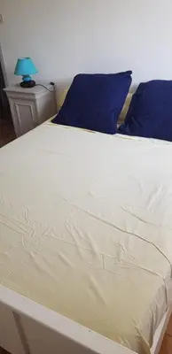 a large white bed with blue pillows and a blue lamp at Charmant T3 en rez de jardin d'une villa in Ghisonaccia