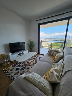 a living room with a couch and a large window at Appartement terrasse spacieuse, vue mer & clim in Ajaccio