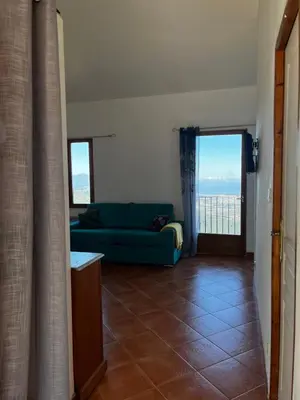 a living room with a blue couch and a balcony at Gîtes la fontaine corse vue panoramique in Loreto-di-Casinca