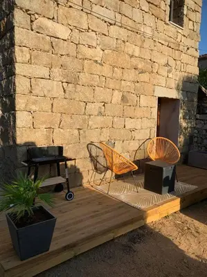 two chairs and a table on a wooden deck next to a brick wall at Caseddu au coeur du village in Monacia-dʼAullène