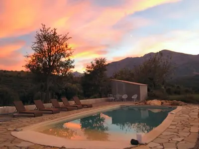 a swimming pool with chairs and a sunset in the background at Appartements de Charme in Corte