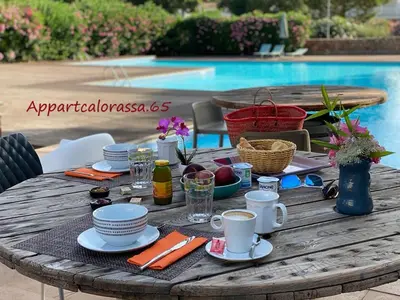 a wooden table with plates and cups on it next to a pool at Appart Cala Rossa - Porto-Vecchio - Mer à pied in Lecci