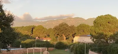 a garden with trees and a building and mountains at Appart Cala Rossa - Porto-Vecchio - Mer à pied in Lecci