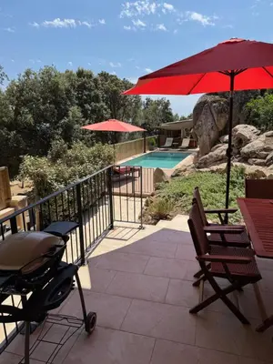 a patio with a red umbrella and chairs and a pool at Bel appartement dans Villa avec piscine en Corse du Sud in Grossa