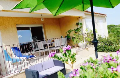 a balcony with a green umbrella and a table and chairs at Villa à Pinarello-2mn à pied de la plage-vue mer in Pinarellu