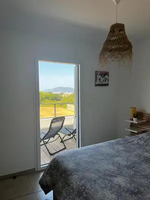 a bedroom with a bed and a balcony with a chair at La Lond'ella - Appt à 1,5km de la mer à Porticcio in Grosseto-Prugna