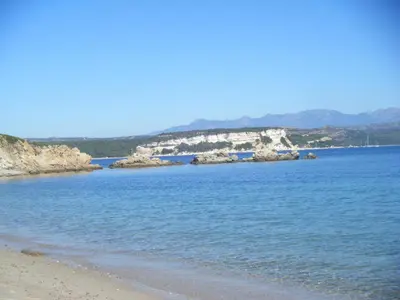 a beach with blue water and a rocky island at Gîte Acellu in Bonifacio