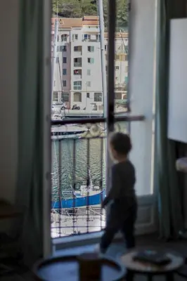 a small child walking through a window looking at a marina at Appartement vue sur le port - Chez Carlu in Bonifacio