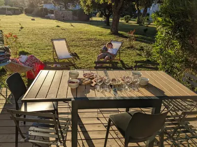 a picnic table with wine glasses and a woman sitting in a chair at Maison/appartement proche Cala Rossa in Lecci