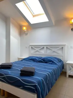 a bedroom with a bed with blue sheets and a skylight at Saint-Florent Appartement duplex in Oletta