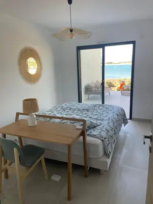 a bedroom with a bed and a table and a window at Le Galatee -T2 luxe les pieds dans l'eau - Porticcio in Porticcio