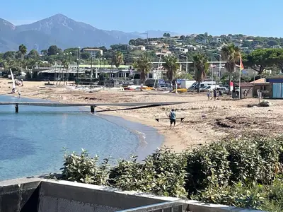 a person walking on a beach with two surfboards at Le Galatee -T2 luxe les pieds dans l'eau - Porticcio in Porticcio