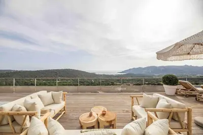 a patio with white couches and tables and an umbrella at Ivona Vacances - Villa de luxe avec piscine chauffée à Santa-Giulia in Porto-Vecchio