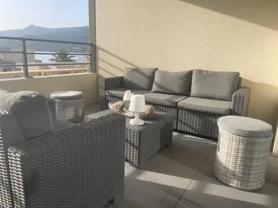 a patio with wicker chairs and a couch on a balcony at Splendide T3 neuf au bord de la plage in Propriano