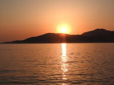 a sunset over the water with mountains in the background at Splendide T3 neuf au bord de la plage in Propriano