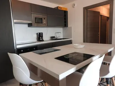a kitchen with a counter with white chairs and a table at Splendide T3 neuf au bord de la plage in Propriano
