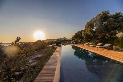 a swimming pool with benches and the sunset in the background at Villa Sud Corse 6ch piscine 27m, accès mer in Pianottoli-Caldarello
