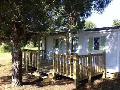 a white house with a porch and a tree at Camping Miami plage in Poggio-Mezzana