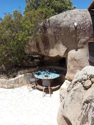 a patio with a table and chairs next to a large rock at Bergerie U Caseddu in Pianottoli-Caldarello